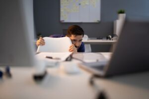 Frightened Businessman Hiding Behind Chair At Workplace
